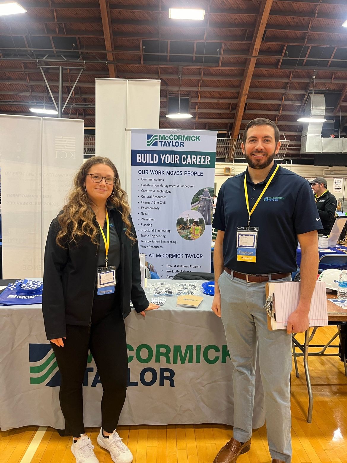 Two employees standing in front of a table at a university career fair.